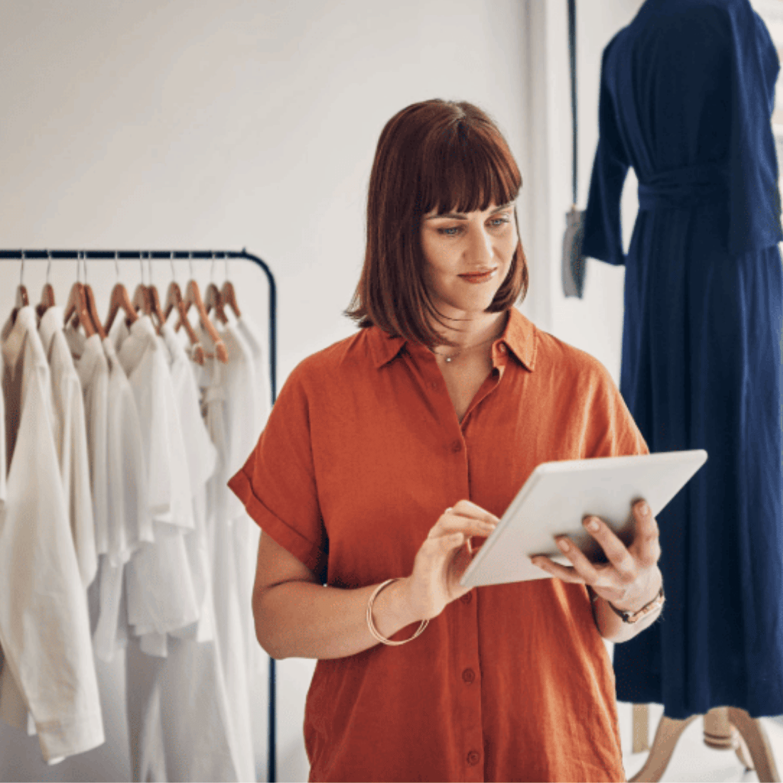 Femme en chemise orange utilisant une tablette dans un magasin de vêtements.