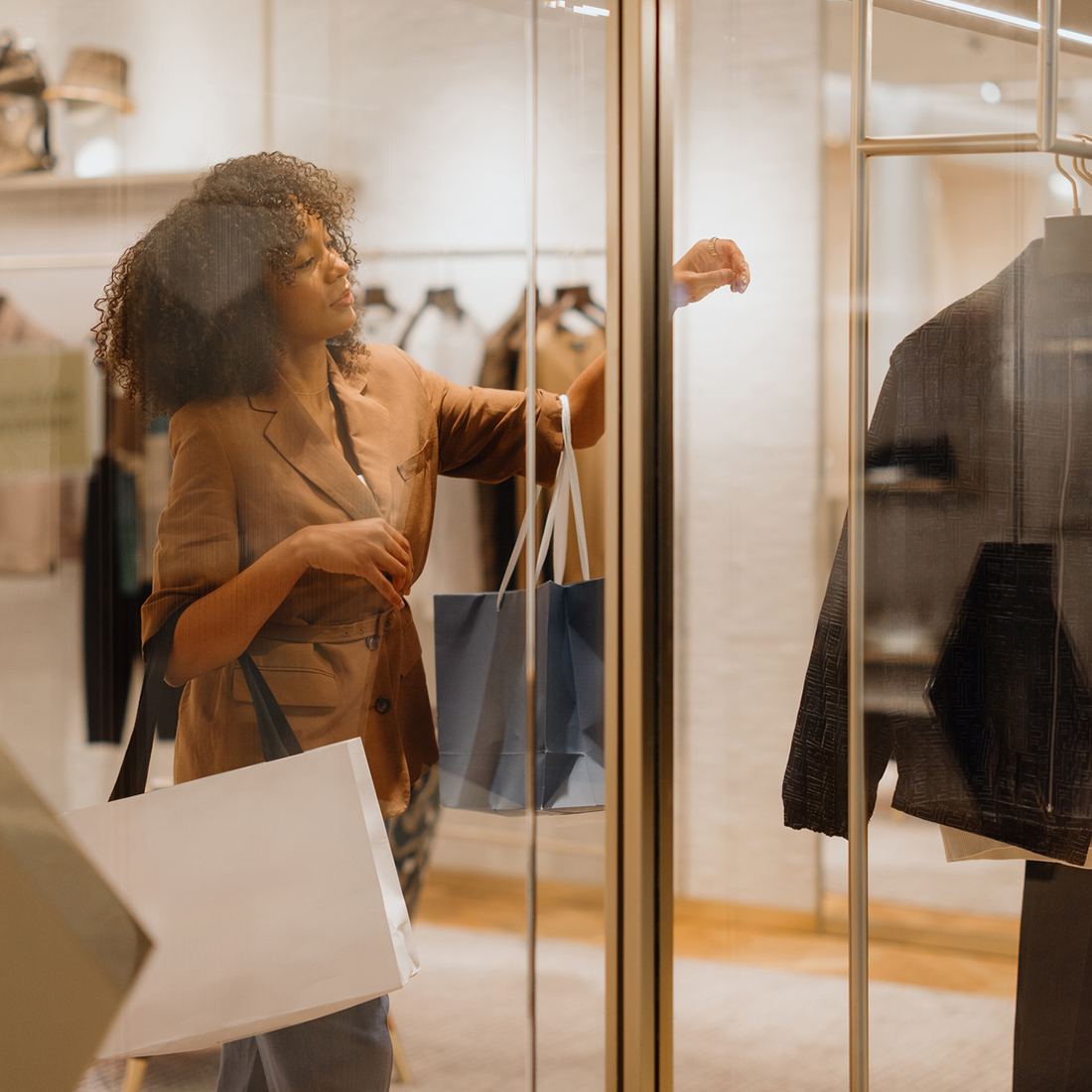 Femme avec sacs de shopping regardant des vêtements exposés dans une vitrine de magasin.