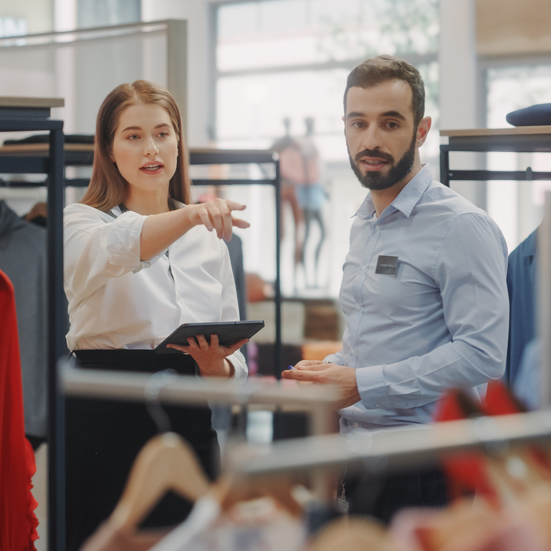 Deux employés dans un magasin discutent, une femme montre quelque chose en tenant une tablette.