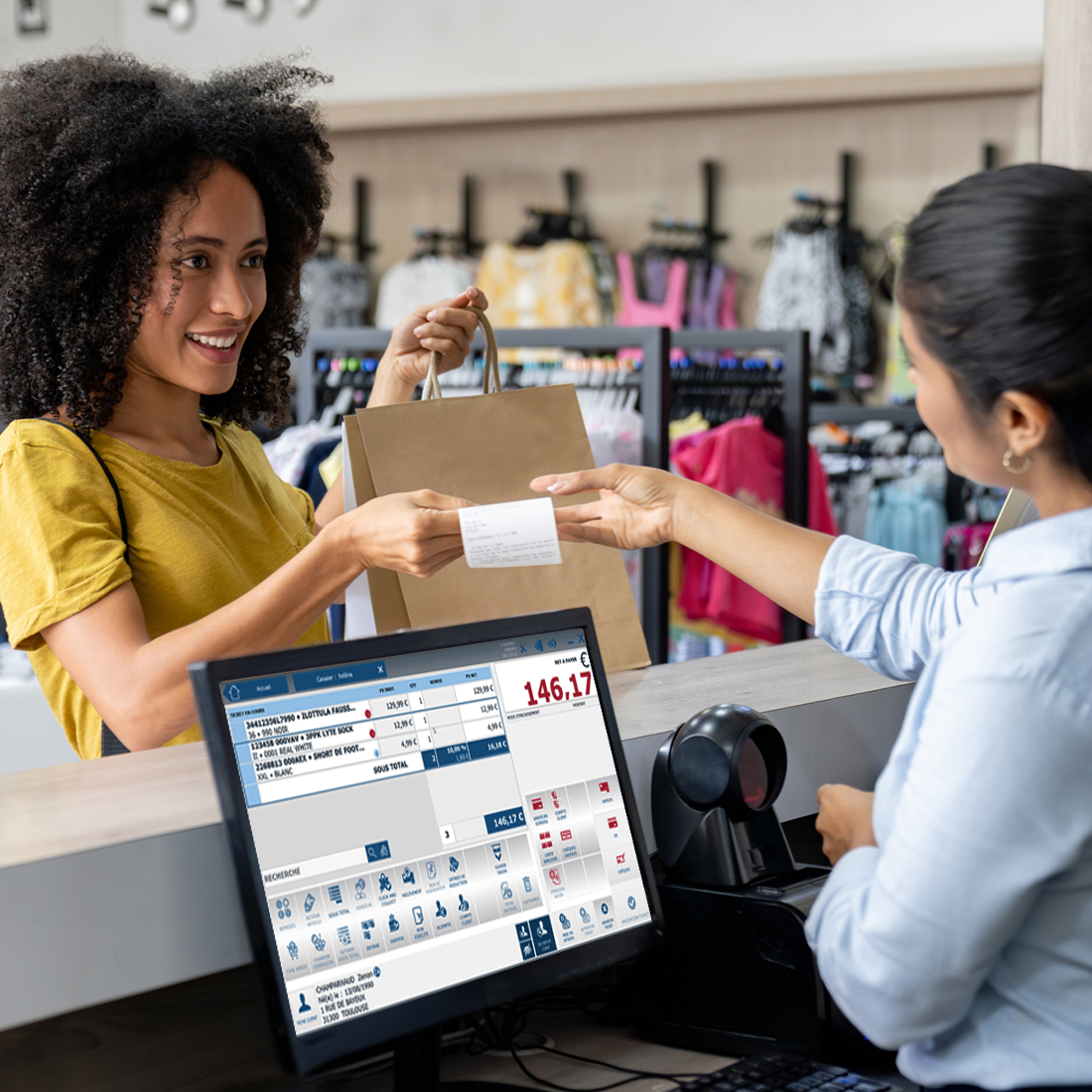 Une cliente souriante reçoit un ticket de caisse tout en tenant un sac dans une boutique de vêtements.