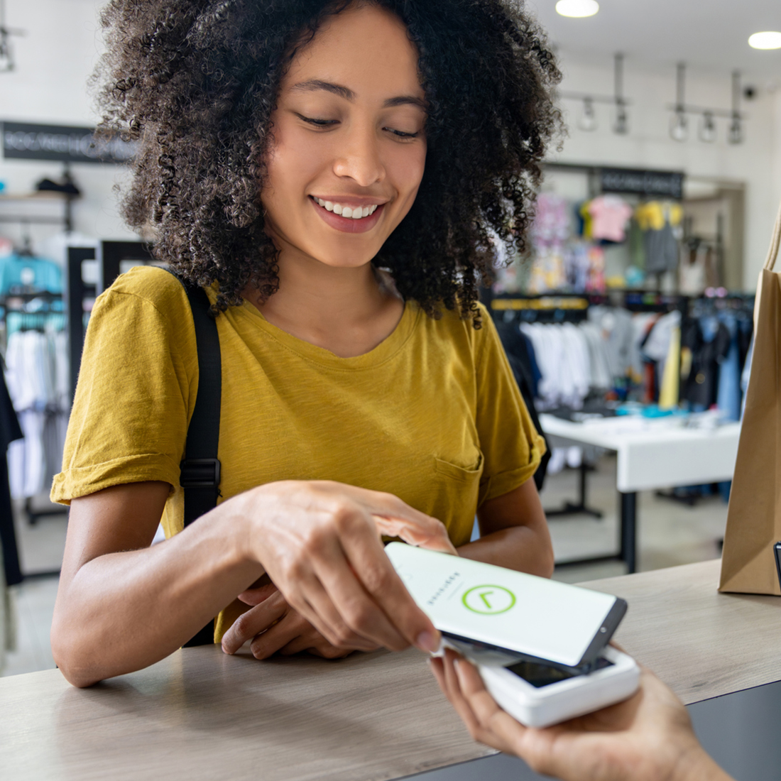 Jeune femme souriante effectuant un paiement sans contact avec un smartphone en boutique.