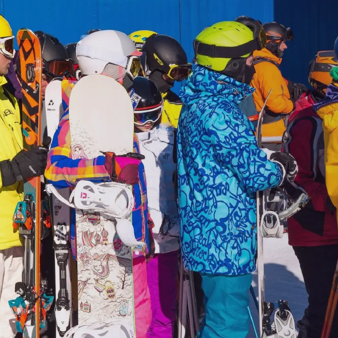 Gens habillés en vêtements de ski et snowboards faisant la queue sur neige au soleil.