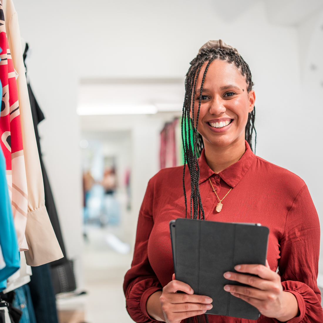Femme souriante tenant une tablette dans une boutique de vêtements lumineuse.