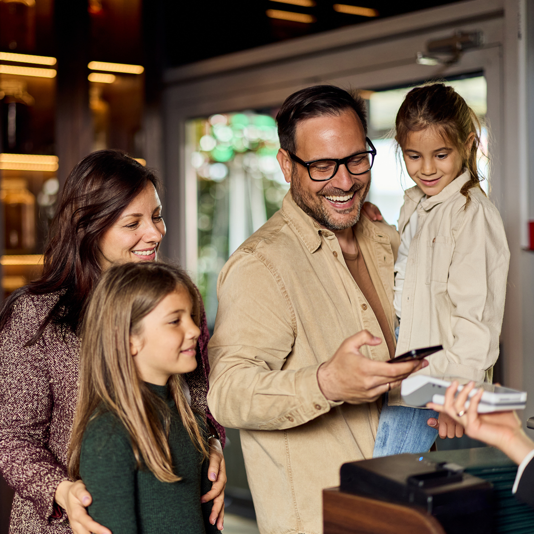 Une famille souriante effectue un paiement sans contact avec un smartphone dans un magasin.