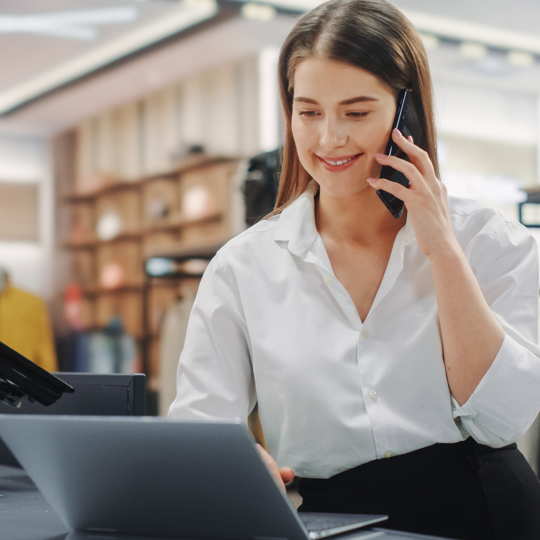 Jeune femme souriante au téléphone utilisant un ordinateur portable dans un espace de travail moderne.