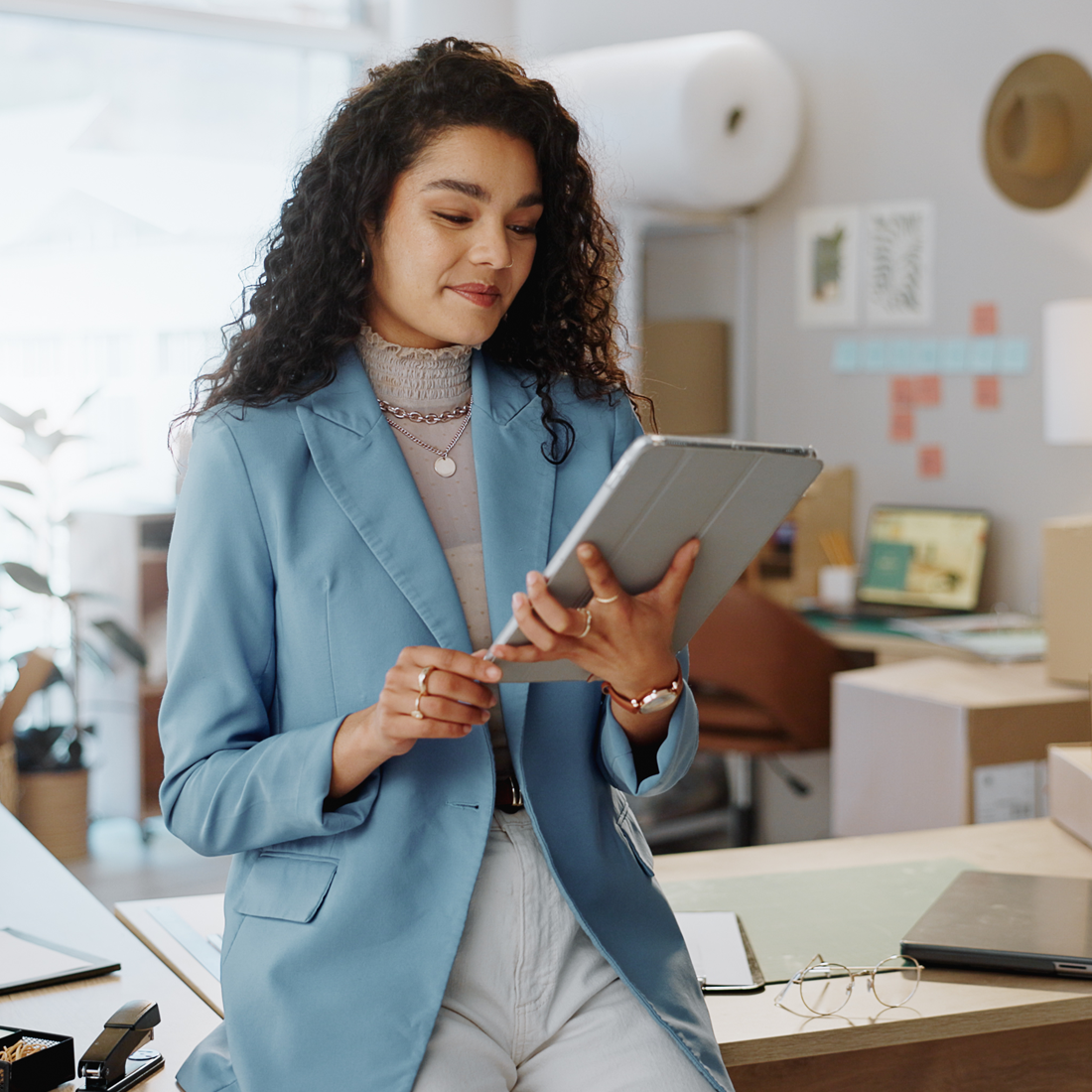 Jeune femme en veste bleue utilise une tablette dans un bureau moderne avec des cartons et un ordinateur portable.