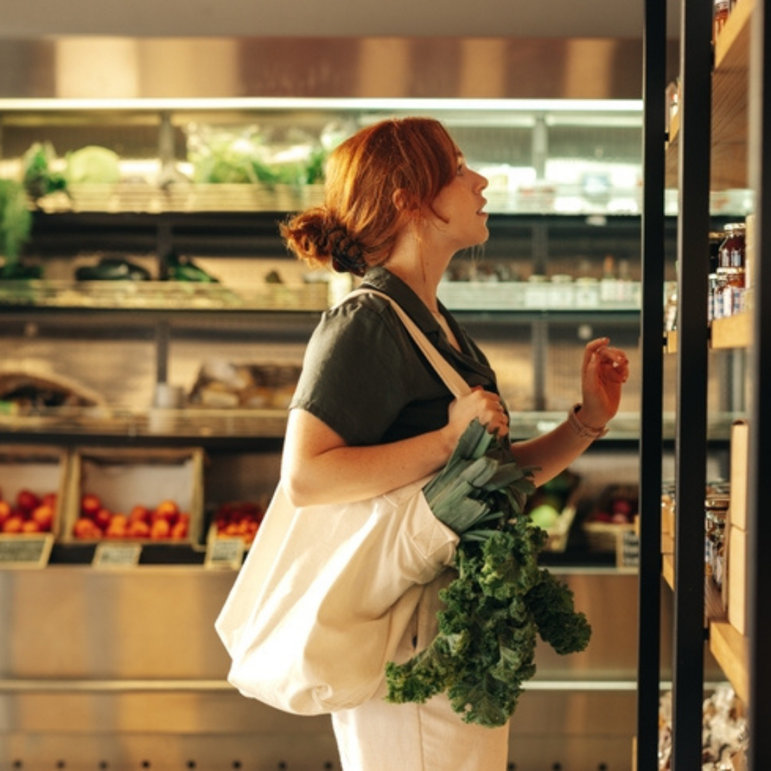 Femme rousse dans un sac en tissu achetant des légumes verts dans une épicerie bio.