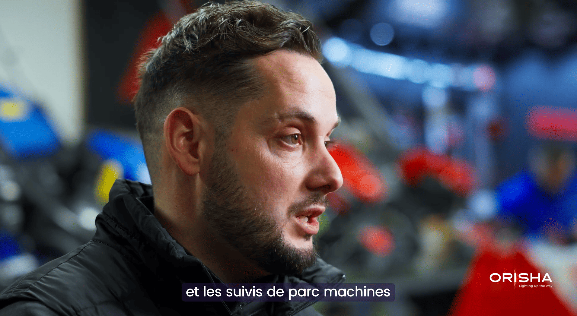 Homme parlant en gros plan, arrière-plan flou avec équipements et logo ORISHA en bas à droite.