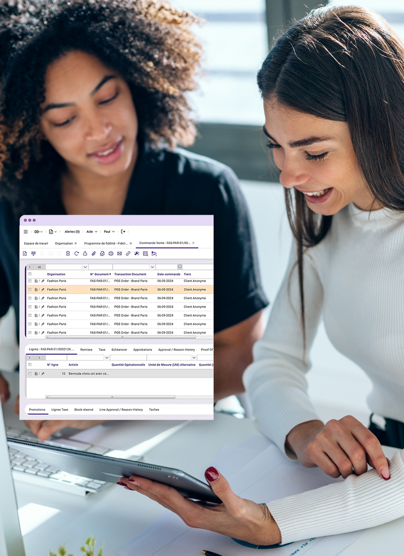 Deux femmes souriantes regardent ensemble un écran d'ordinateur portable montrant un logiciel de gestion.