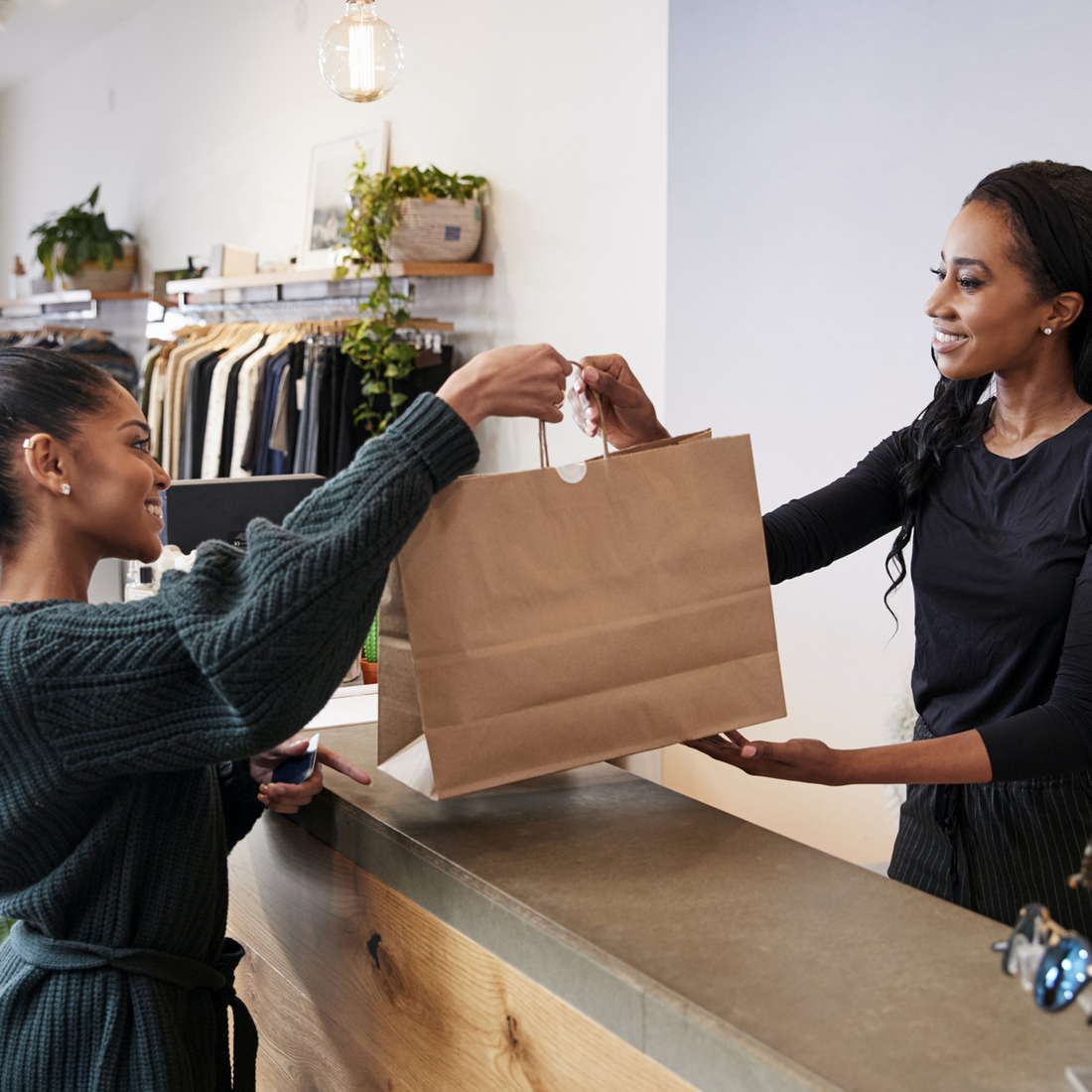 Une vendeuse souriante remet un sac en papier à une cliente au comptoir d'un magasin de vêtements.