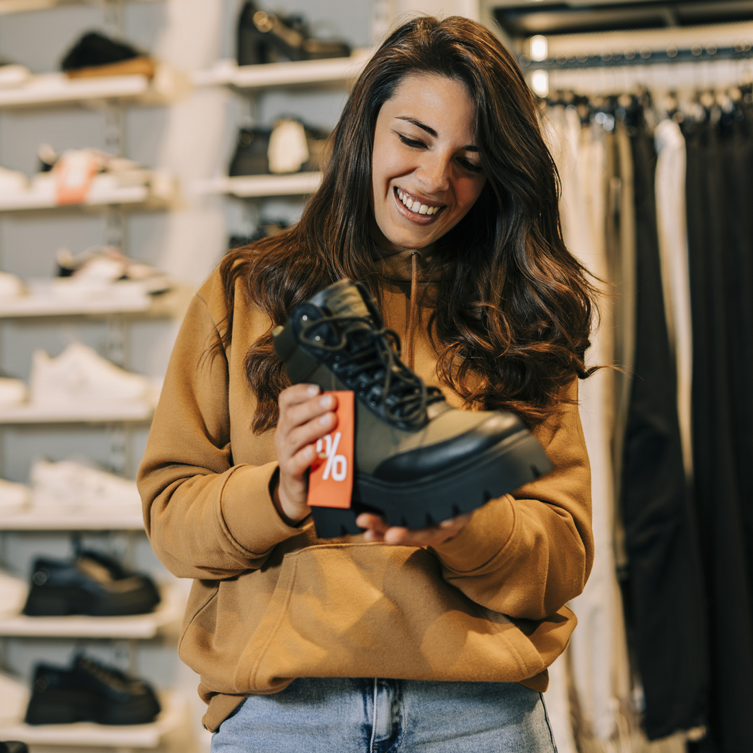 Jeune femme souriante tient une botte noire avec une étiquette de réduction en magasin de chaussures.