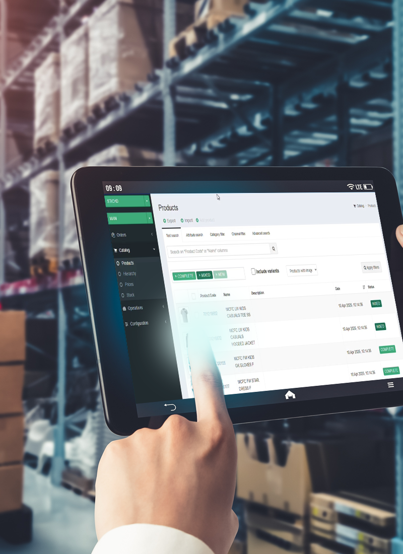 Une main utilise une tablette affichant un logiciel de gestion de produits dans un entrepôt.