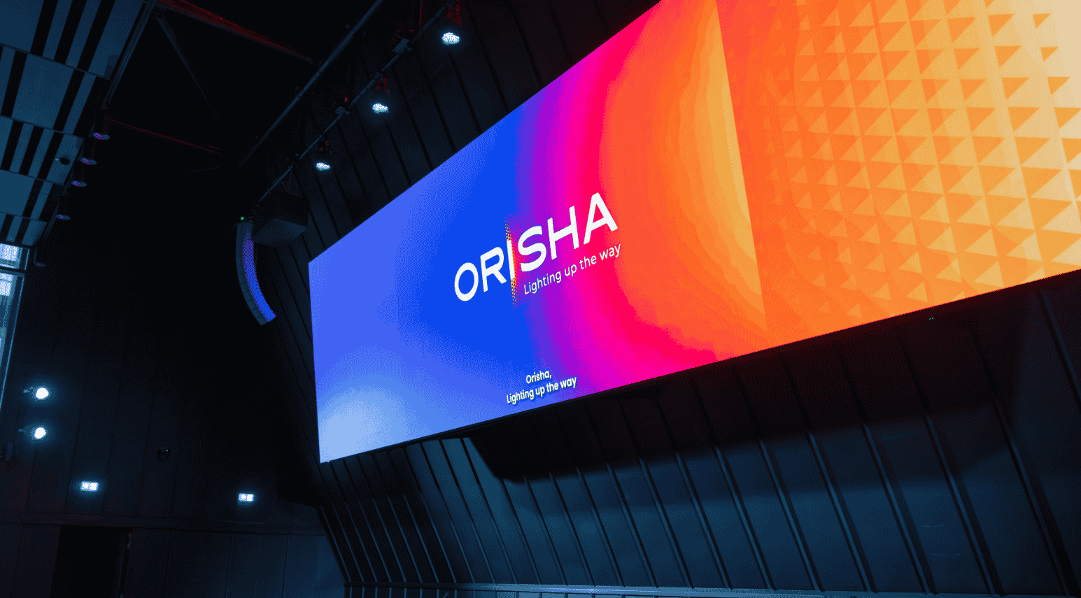 Grand écran lumineux affichant le logo ORISHA avec le slogan « Éclairer le chemin » dans une salle sombre.