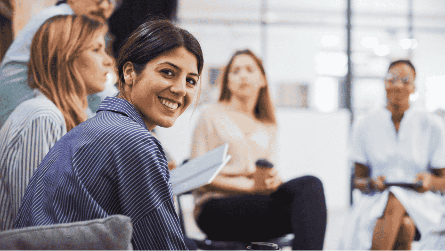 Groupe de femmes en réunion, une souriante regardant vers la caméra, dans un bureau lumineux.