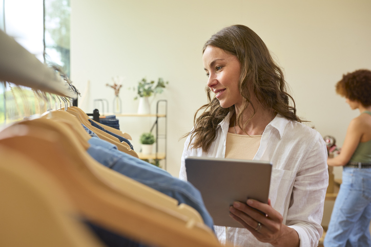 Magasin de vêtement avec ne vendeuse qui tient dans les mains une tablette et utilise un logiciel retail