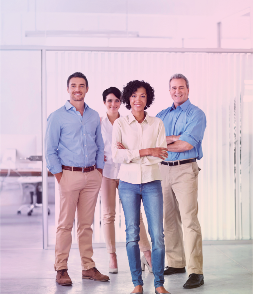 Quatre professionnels souriants debout dans un bureau moderne avec des fenêtres en verre et des stores verticaux, portant des tenues de travail décontractées.